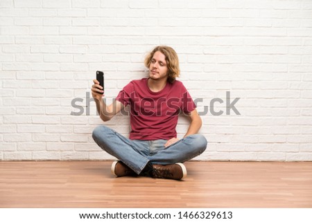Blonde man sitting on the floor making a selfie