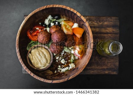 Wooden bowl with falafel balls, hummus and fresh salad. Olive oil in bottle on side. Dark black background, top view. Traditional israeli food. Veganism concept.