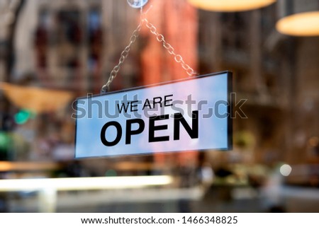 A sign board through the glass of store window. We are open, Sorry we are closed. 