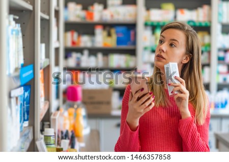 Woman uses smart phone while in pharmacy. They have the best medicine here. They have so much on offer here. Woman Checking Supplement On Smartphone At Pharmacy