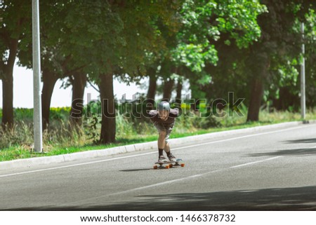 Skateboarder doing a trick near by meadow in sunny day. Young man in equipment riding and longboarding on the asphalt in action. Concept of leisure activity, sport, extreme, hobby and motion.