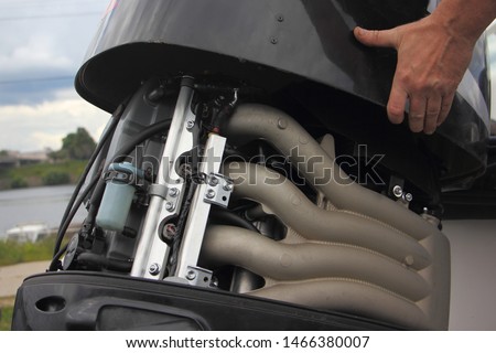 A man's hand closes the hood of a powerful outboard boat motor, repair and maintenance of boat engines, a view of the intake manifold of a four-cylinder four-stroke injector motor Royalty-Free Stock Photo #1466380007