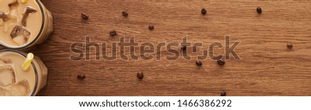 top view of ice coffee in glasses near coffee grains on wooden table, panoramic shot
