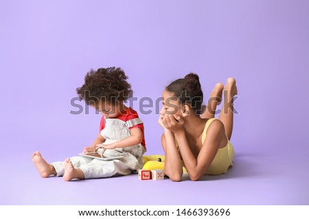 Cute African-American sisters with tablet computer watching cartoons on color background