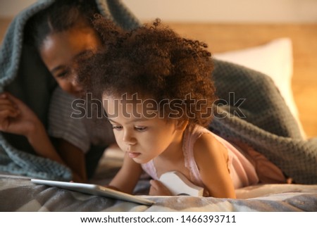 Cute African-American sisters with tablet computer watching cartoons in bedroom