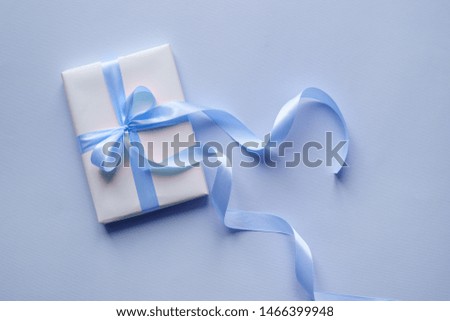 Decorative white gift box with blue bow and long beautiful ribbon on a blue background. Top view
