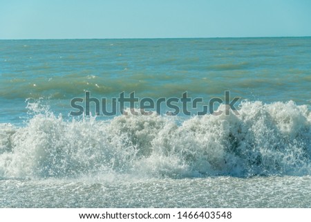 Close-up of sea wave with white foam comes ashore on a sunny day. Waves on the shore of the Black Sea on a sunny day