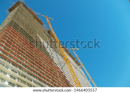 The construction of a multistory building against the blue sky, stands next to a yellow tower crane. Photo down