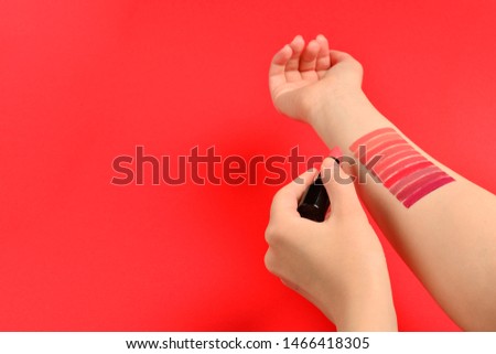 Lipstick swatches on woman hand isolated on red background.