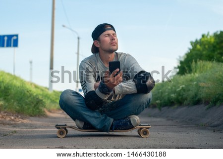 Tired happy young skater dozing sitting on a skateboard, breathing fresh air. People and the concept of relaxation,