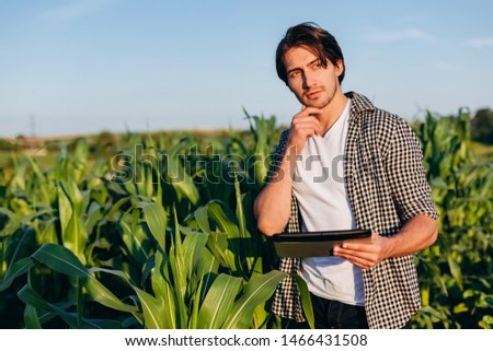 Portrait of thoughtfully agronomist standing in a corn field with ipad and touching his chin