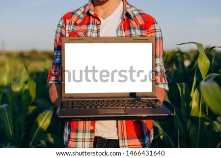 Farmer standing in a field holding open  laptop. White screen mockup