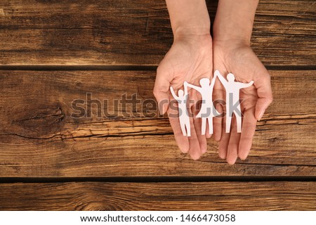 Woman holding paper figures of happy family in hands on wooden background, top view. Space for text