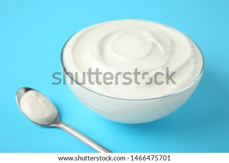 Glass bowl of sour cream and spoon on light blue background