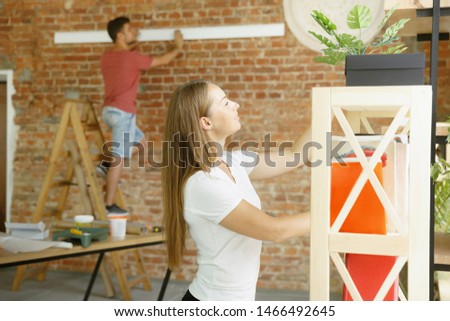 Young couple doing apartment repair together themselves. Married man and woman doing home makeover or renovation. Concept of relations, family, love. Put new furniture and books on the shelves.