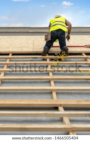 Concept of residential building under construction. Vertical photo mature builder in protective uniform wear standing on rooftop of new modern house. Unrecognizable man working on roof top