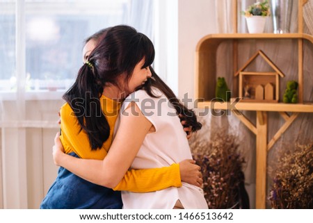 Smiling Asian teenage daughter and Asian middle-aged mother hugging with happy warm expression and tenderness in indoor living room at home. They have good relationship together. Mother's day concept