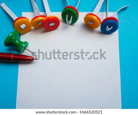 Multi-colored paper clips and a white sheet of paper with a red pen. View from above. Concept back to school. space for text
