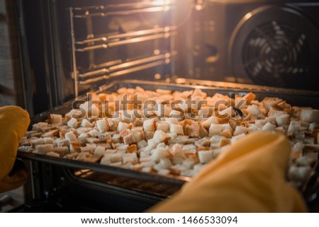 white and black bread croutons put in the oven to cook, yellow oven mitts Royalty-Free Stock Photo #1466533094