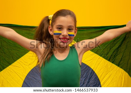 Football supporter, Brazil team. Beautiful little girl cheering for her team on yellow background