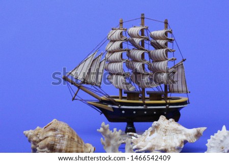 Toy ship on a blue background. Near many seashells. Ship model. Sailboat. Cruise.