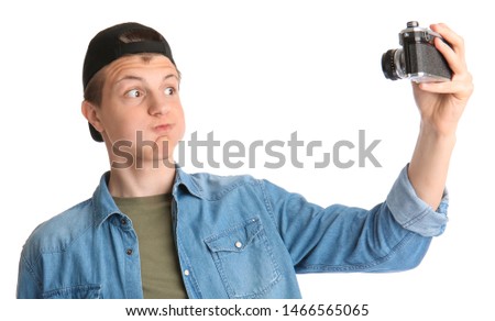 Teenage boy with photo camera taking selfie on white background