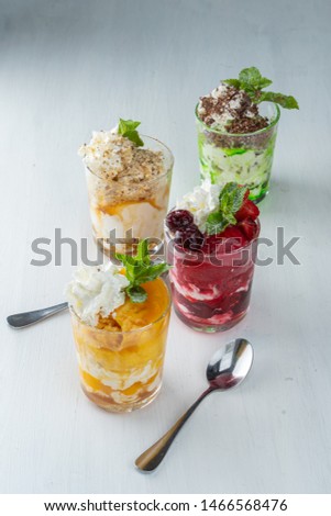 Assortment of ice cream layered desserts on a white background: vanilla ice cream with various toppings – berries, orange, mango, nuts and chocolate chips