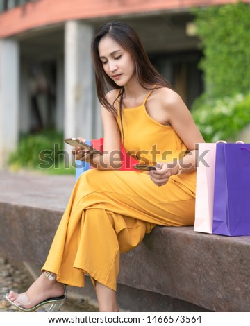 Young Asian womanshow her credit card and smiling,she is sitting and looking at it,uses a mobile to shopping online,Close to many colored paper bags