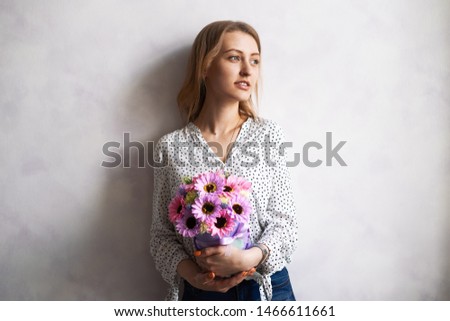 Beautiful girl with a large multicolored bouquet of flowers stands against the wall.