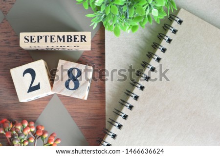 September 28. Date of September month. Number Cube with a flower and notebook on Diamond wood table for the background.