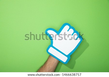 cropped view of man holding paper icon of thumb up on green