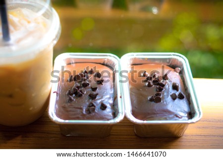 Close up of a chocolate fudge cake in square foil baking cups on  wood table in cafe. And blur image of bokeh tree green and golden light color background. 