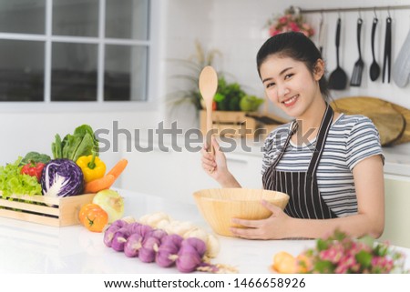 Beautiful asian woman is showing wooden spatula in the bright white kitchen. wife or housewife is preparing to cook food which consists of a variety of fruits and vegetables for the family.