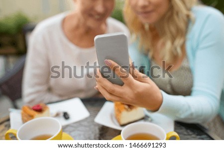 family, technology and people concept - close up of happy smiling adult daughter and senior mother with smartphone taking selfie at cafe