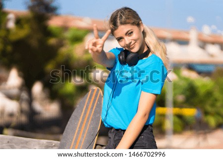Teenager girl with skate at outdoors smiling and showing victory sign
