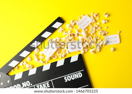 Flat lay composition with clapperboard, popcorn and tickets on yellow background