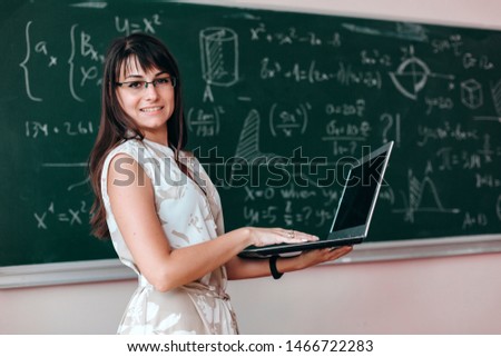 Woman teacher in glasses holding open laptop and looking at the camera. Back to school