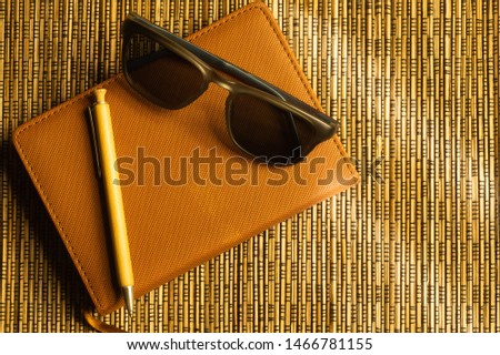 Diary and pen with sunglasses on a wooden bamboo background. notebook and pen top view. copy space