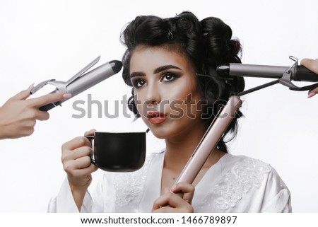Girl with curlers in bathrobe. Beauty portrait. Close-up of brunette girl enjoy coffee. Surrounded by many hands holding curling and straightening iron. Morning preparation. 