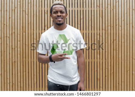 Young attractive man in t-shirt with recycle symbol on wooden background. Eco symbol.
