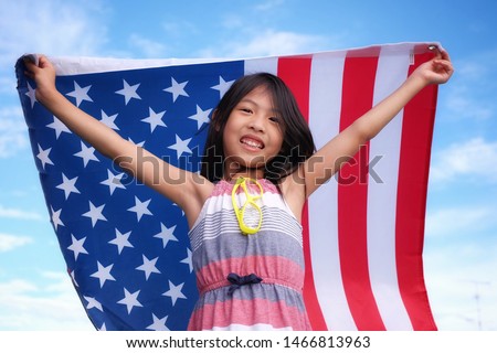 An Asian American girl proudly holding an American flag in the air with clear blue sky, happy and smiling on 4th of July, Independence day, Memorial day 