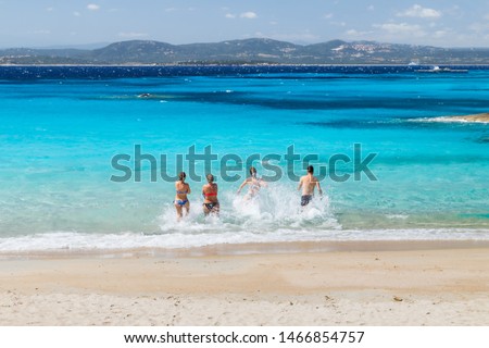 Group of friends running into the sea in a sunny summer day, freedom and travel concept. Summer holidays on the beach. Sardinia, Italy.