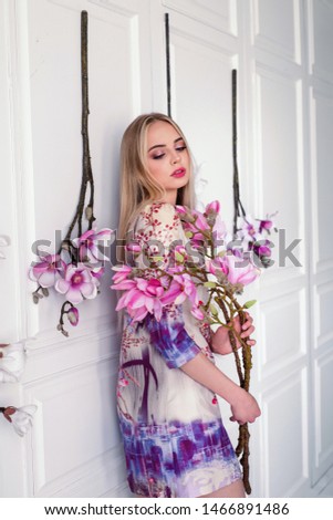 Beautiful  woman model with long blond hair wearing  dress,posing in interior studio with flowers.