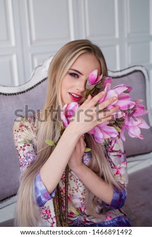Beautiful smiling woman model with long blond hair wearing  dress,posing in interior studio with flowers.