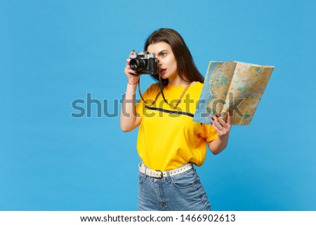 Attractive young woman in vivid casual clothes take pictures on retro vintage photo camera hold paper city map isolated on blue wall background in studio. People lifestyle concept. Mock up copy space