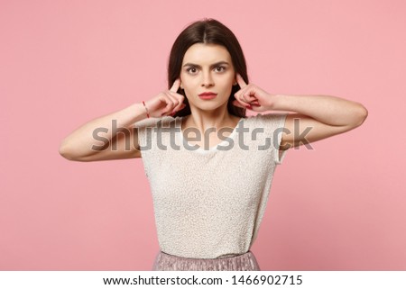 Serious young woman in casual light clothes posing isolated on pastel pink wall background studio portrait. People sincere emotions lifestyle concept. Mock up copy space. Covering ears with fingers