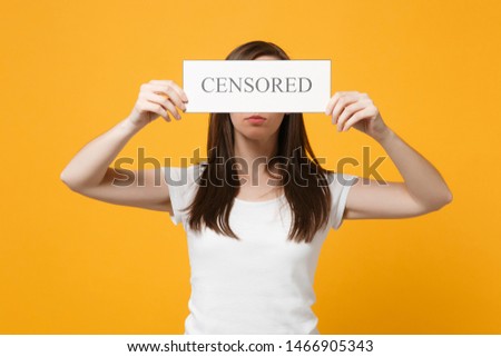 Portrait of young woman in white casual clothes covering eyes holding sign with censored title isolated on bright yellow orange wall background in studio. People lifestyle concept. Mock up copy space