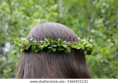 A wreath of leaves.Rear view of a girl with a wreath on her head.Beautiful picture Woven leaves of berry bushes on long dark hair of natural color. Neat hairstyle on abstract green background close up