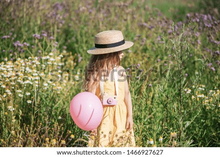 Cute little girl walking in the flowers field in yellow dress and hat, summer time