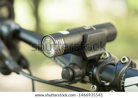 A small black flashlight for a safe night ride, mounted on the handlebars of the bicycle. Convenient and useful gadget for bike cyclist. Close-up photo on nature background